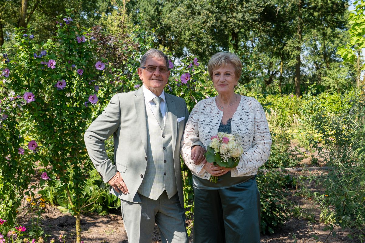 Un couple de seniors élégant pose dans un jardin fleuri, elle tient un bouquet