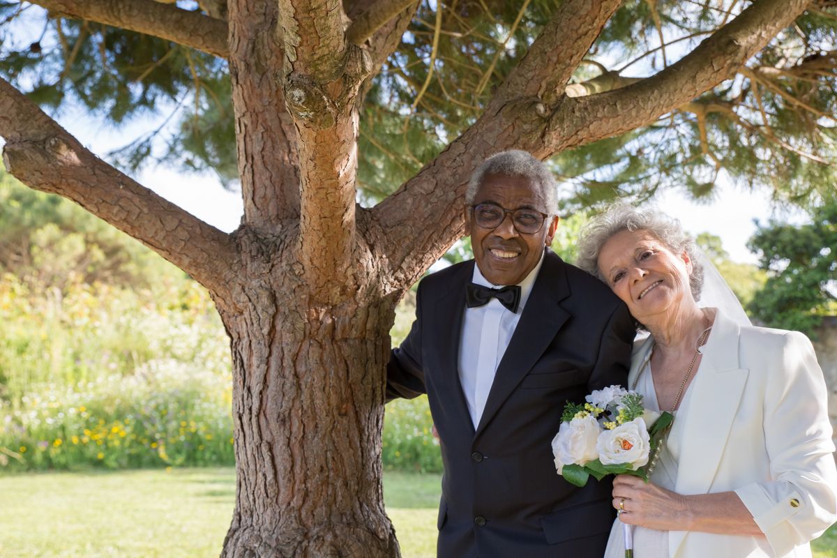 Un couple de seniors élégamment habillé pose sous un arbre