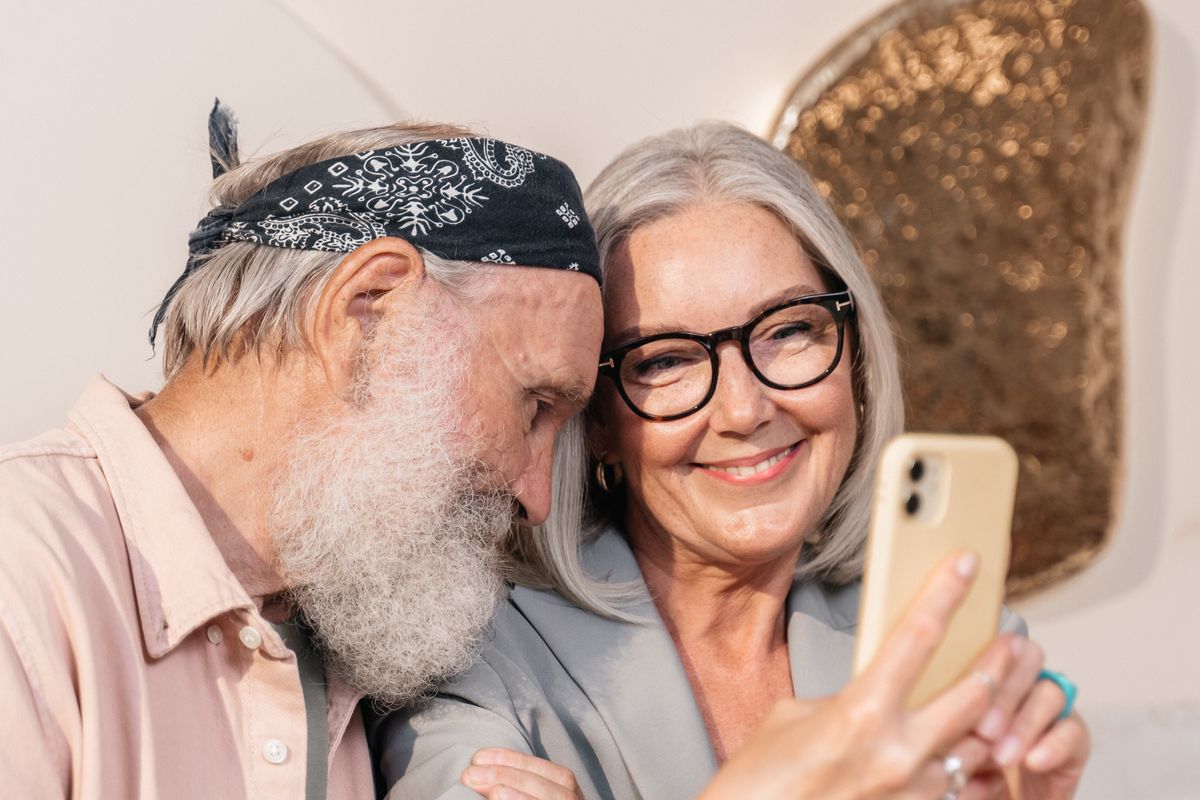 Et smilende ældre par tager et billede med en smartphone